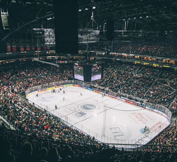 En vid utsikt over en fullpakket ishockeyarena med spillere på isen og et stort poengsumtavle.