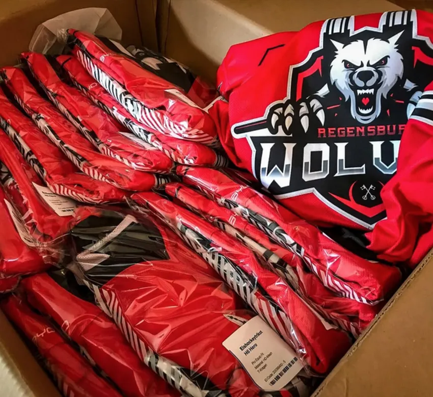 En pappeske med flere røde, tilpassede sportskjoler pakket i plast, en av dem med et ulvemotiv og teksten 'REGENSBURG WOLVES'.