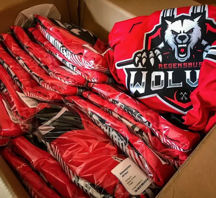 En pappeske med flere røde, tilpassede sportskjoler pakket i plast, en av dem med et ulvemotiv og teksten 'REGENSBURG WOLVES'.