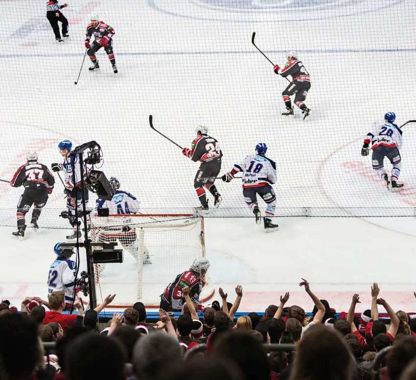 En dynamisk ishockeyscene med spillere i aksjon på isen og en heiarende mengde i bakgrunnen.