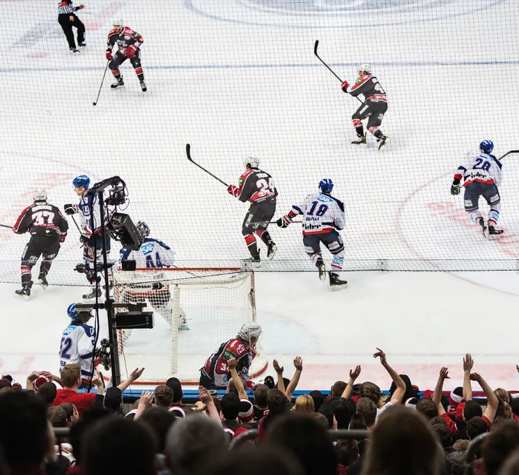 En dynamisk ishockeyscene med spillere i aksjon på isen og en heiarende mengde i bakgrunnen.