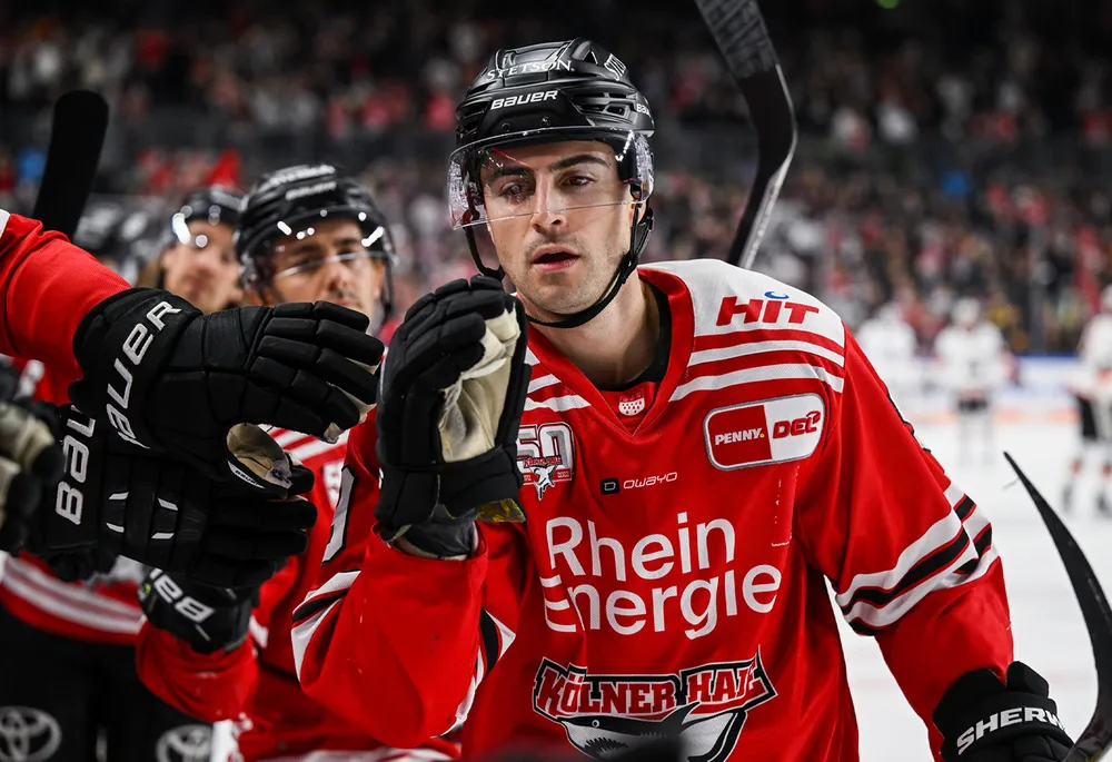 En ishockeyspiller i rød drakt med svarte hansker og hjelm, som feirer med lagkamerater.