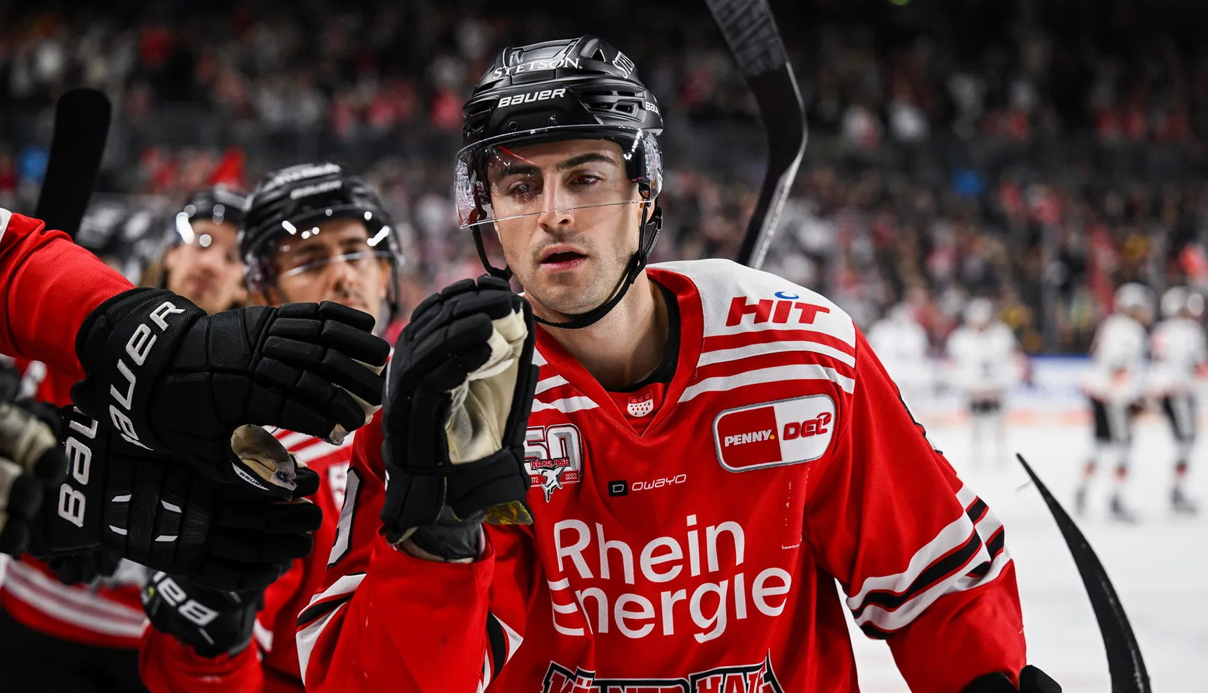 En hockeyspiller i en rød trøye med hvite striper og hansker, som reagerer under kampen.