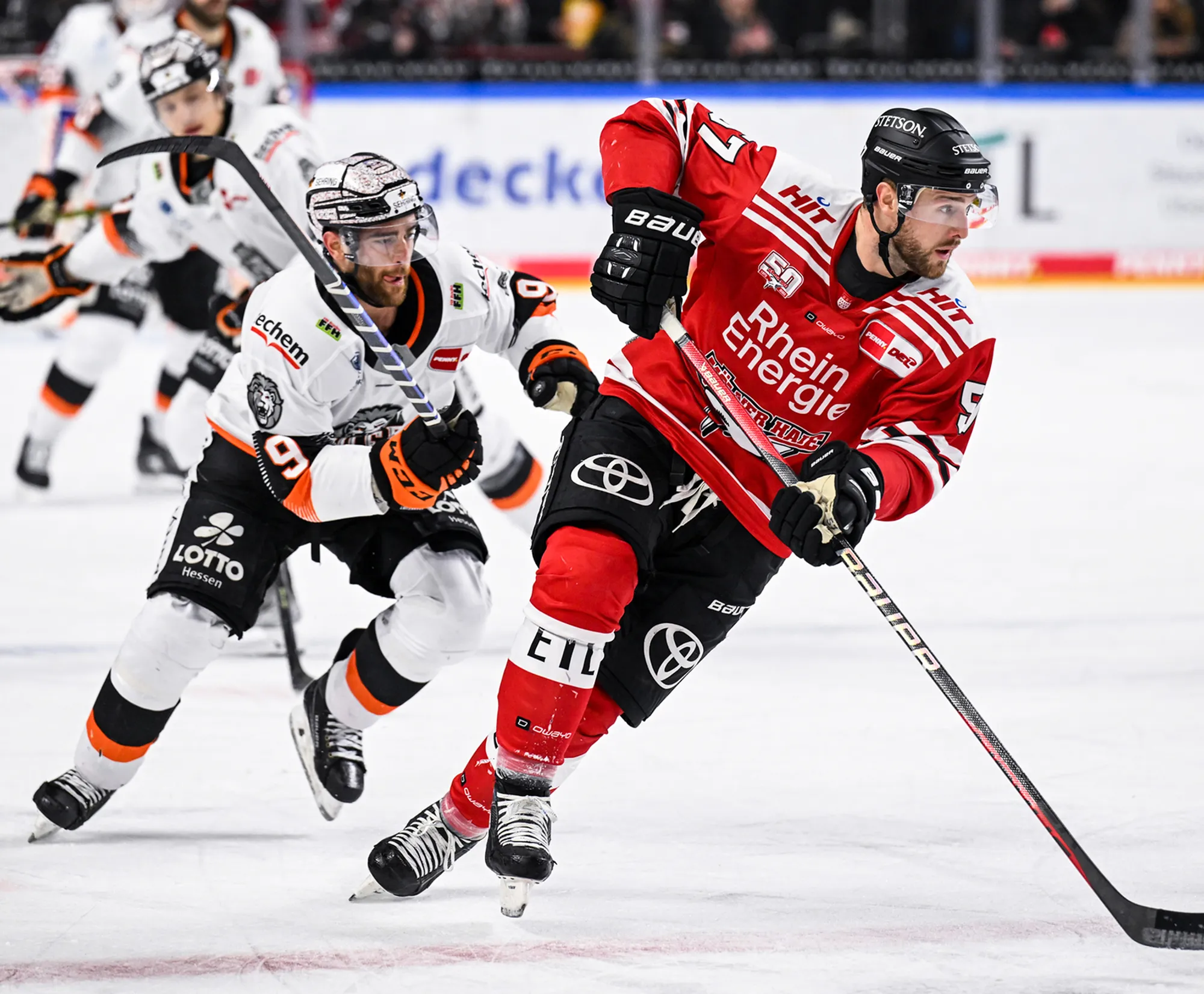 To ishockeyspillere på isen, den ene i rød trøye og den andre i hvit trøye med oransje detaljer.
