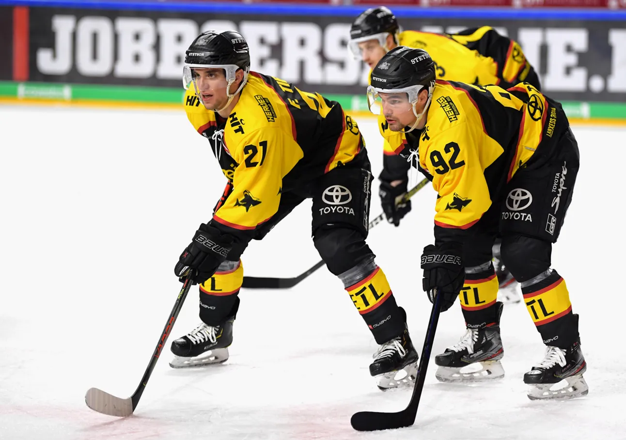 To ishockeyspillere i gule og svarte drakter med nummer 21 og 92 på isen, fokusert på spillet.