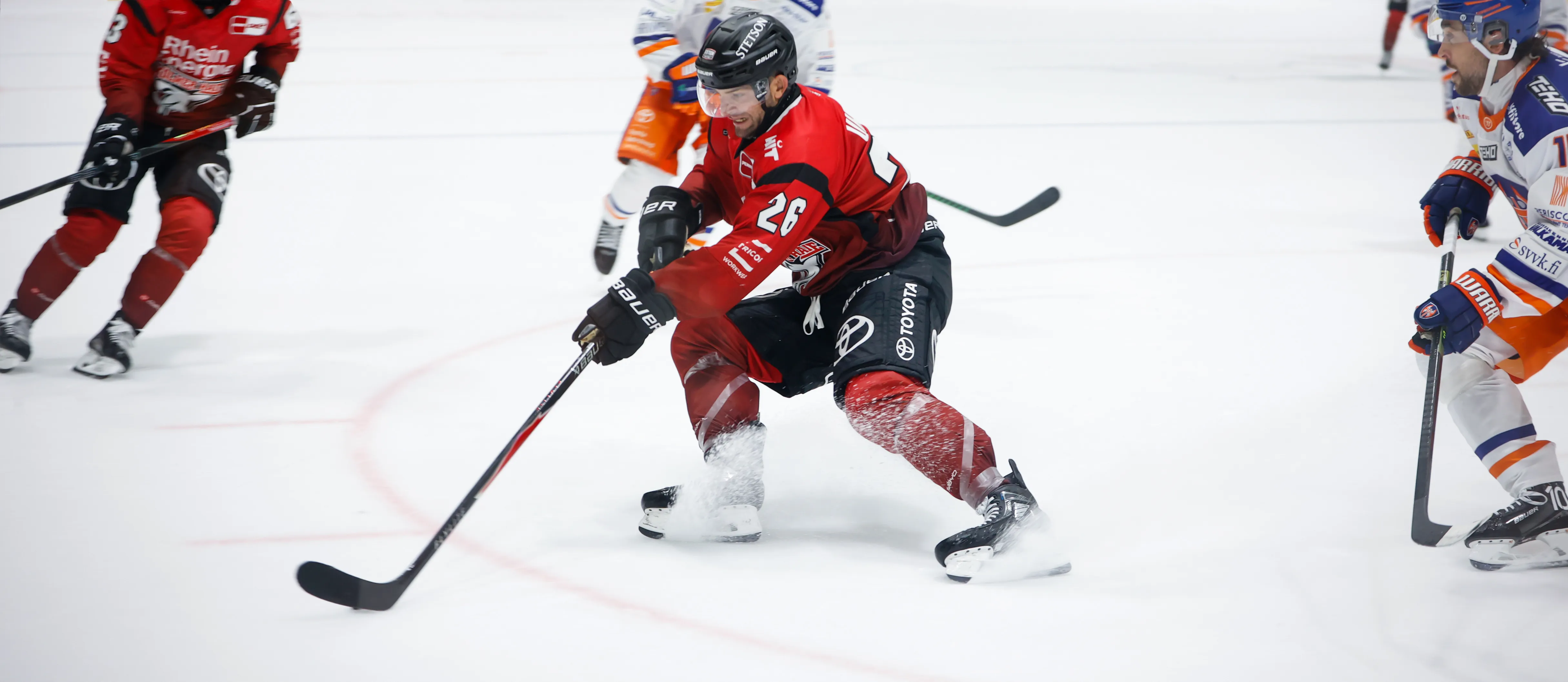 En ishockeyspiller i rød sportsklær dribler pucken på isen.