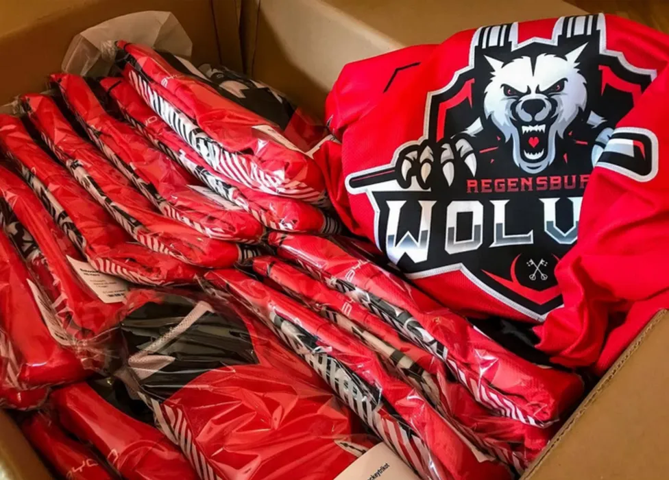 En boks med røde, tilpassede sportskjoler, inkludert en med et ulvemotiv og teksten 'Regensburg Wolves'.