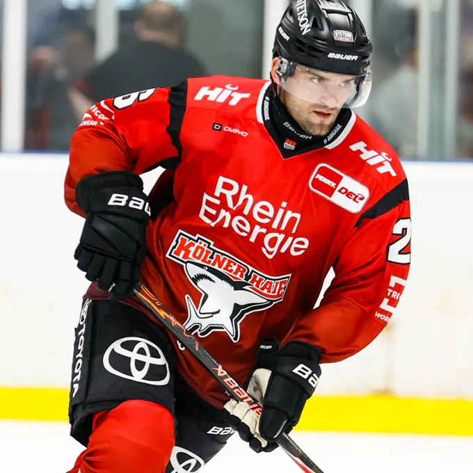 En ishockeyspiller i en rød trøye med logoen til Rhein Energie og Kölner Haie, på isen.