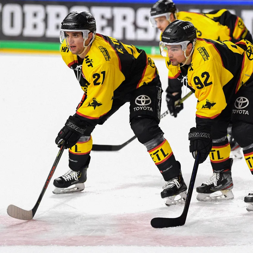 To ishockeyspillere i gule og svarte trøyer er på isen.