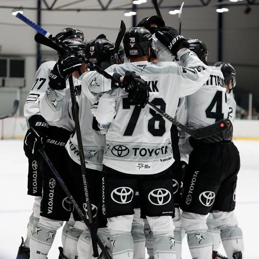 En gruppe ishockeyspillere i hvite og svarte drakter omfavner hverandre på isen.