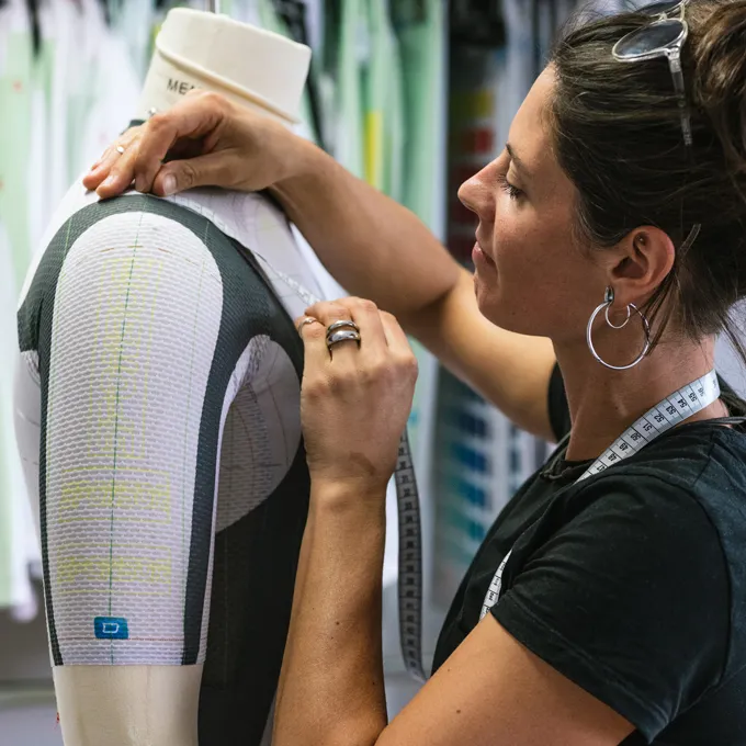 En kvinne justerer et tilpasset sportsutstyr på en mannequin mens hun har et målebånd rundt halsen.