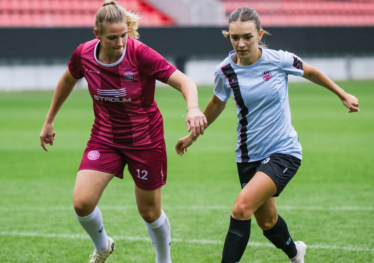 To kvinnelige fotballspillere i fargerike drakter som interagerer på et gressfelt.