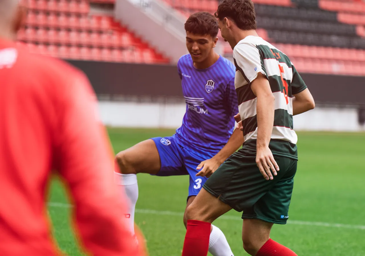 To fotballspillere i aksjon på banen, en iført en blå trøye og den andre en grønn og hvitstripet trøye.