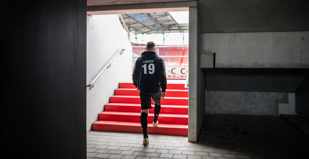 En atlet som har på seg en svart hettegenser med nummer 19 og korte bukser går opp de røde trappene i en stadion.
