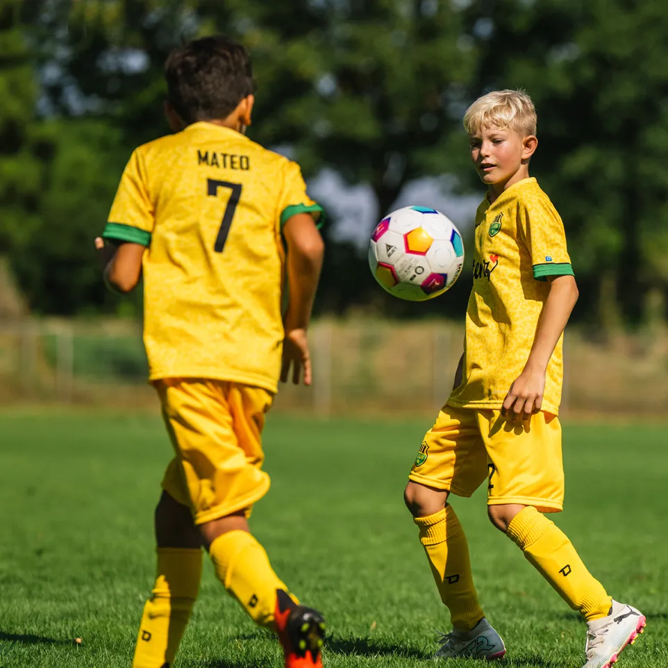 To barn i gule fotballtrøyer og shorts spiller på en grønn fotballbane.
