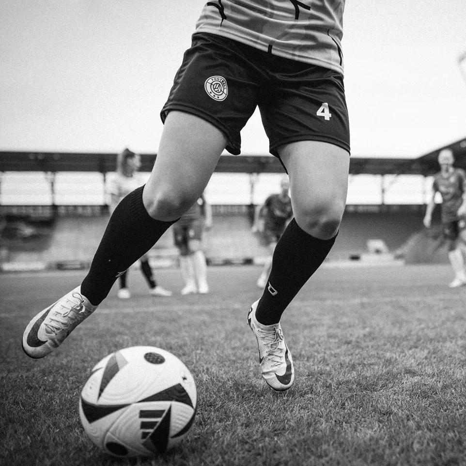 En spiller i shorts og strømper som dribler en fotball på et gressfelt.