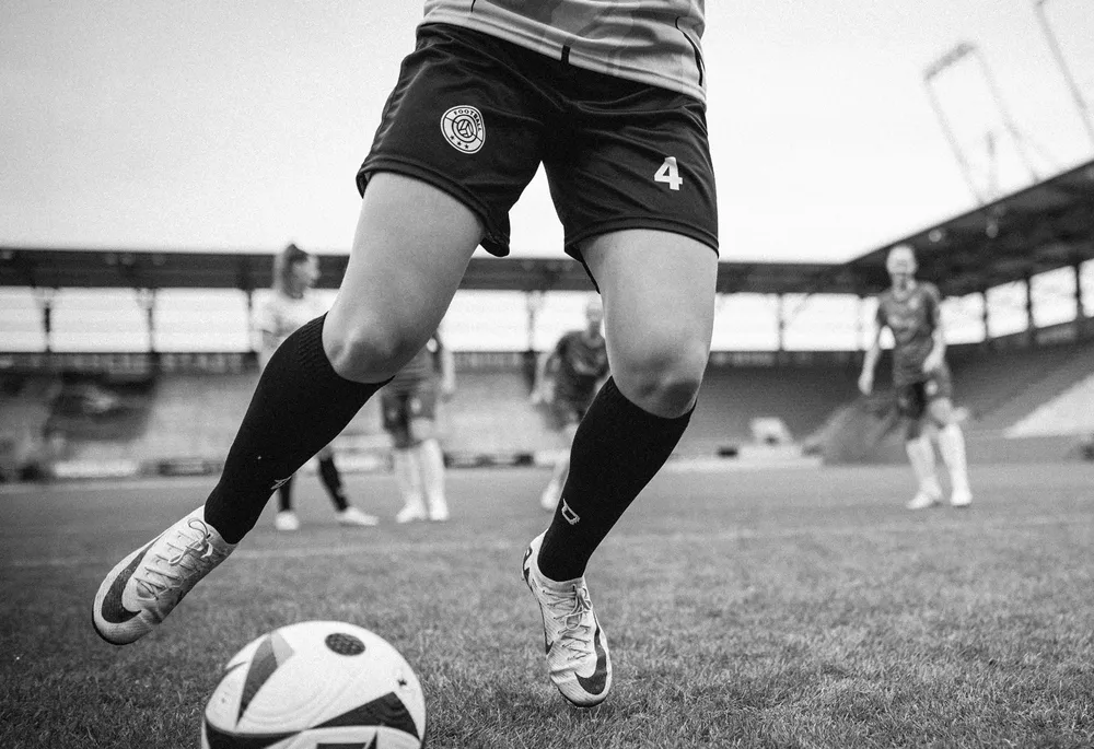 En kvinnelig spiller i korte fotballshorts og lange sokker dribler en ball på banen.