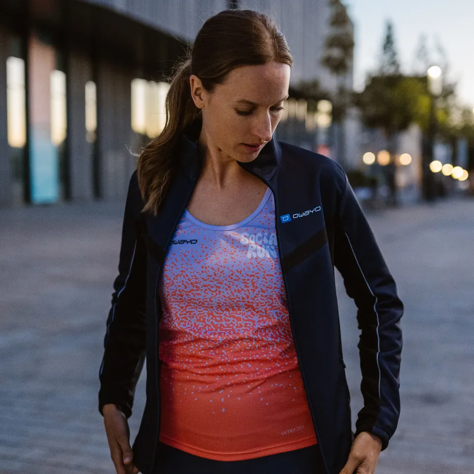En kvinne har på seg en sporty jakke og en fargerik ermeløs topp med et moderne design mens hun står på en urban gate.