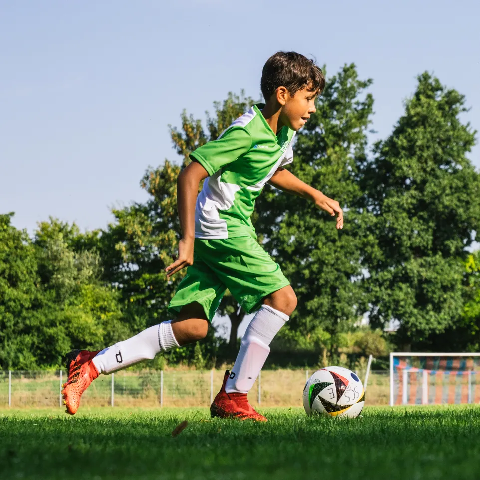 En ung fotballspiller i grønn og hvit sportsdrakt løper på en fotballbane.