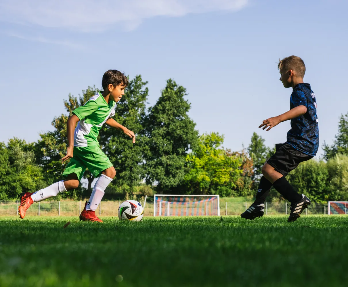 En ung fotballspiller i grønn trøye løper med ballen på en gressbane.