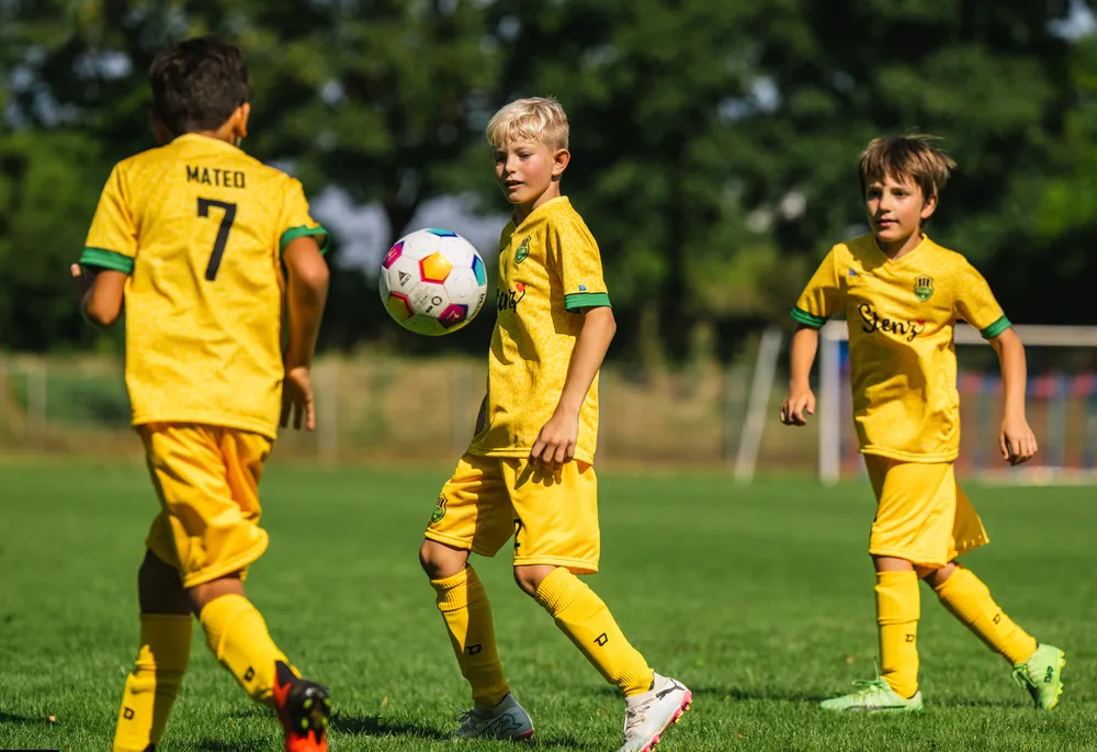 Tre barn i lysegule fotballtrøyer spiller på en gressbane.