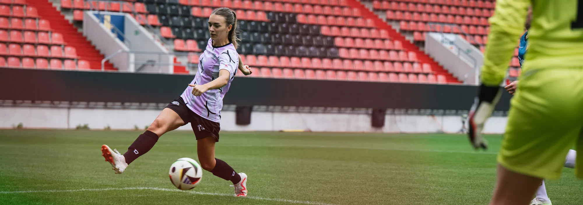 En kvinnelig spiller i en lilla fotballtrøye kicker ballen på en gressbane.