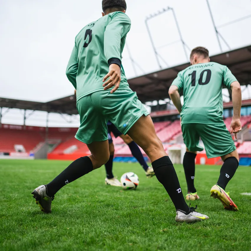 To fotballspillere i grønne trøyer og svarte sokker som spiller på en gressbane med en ball.