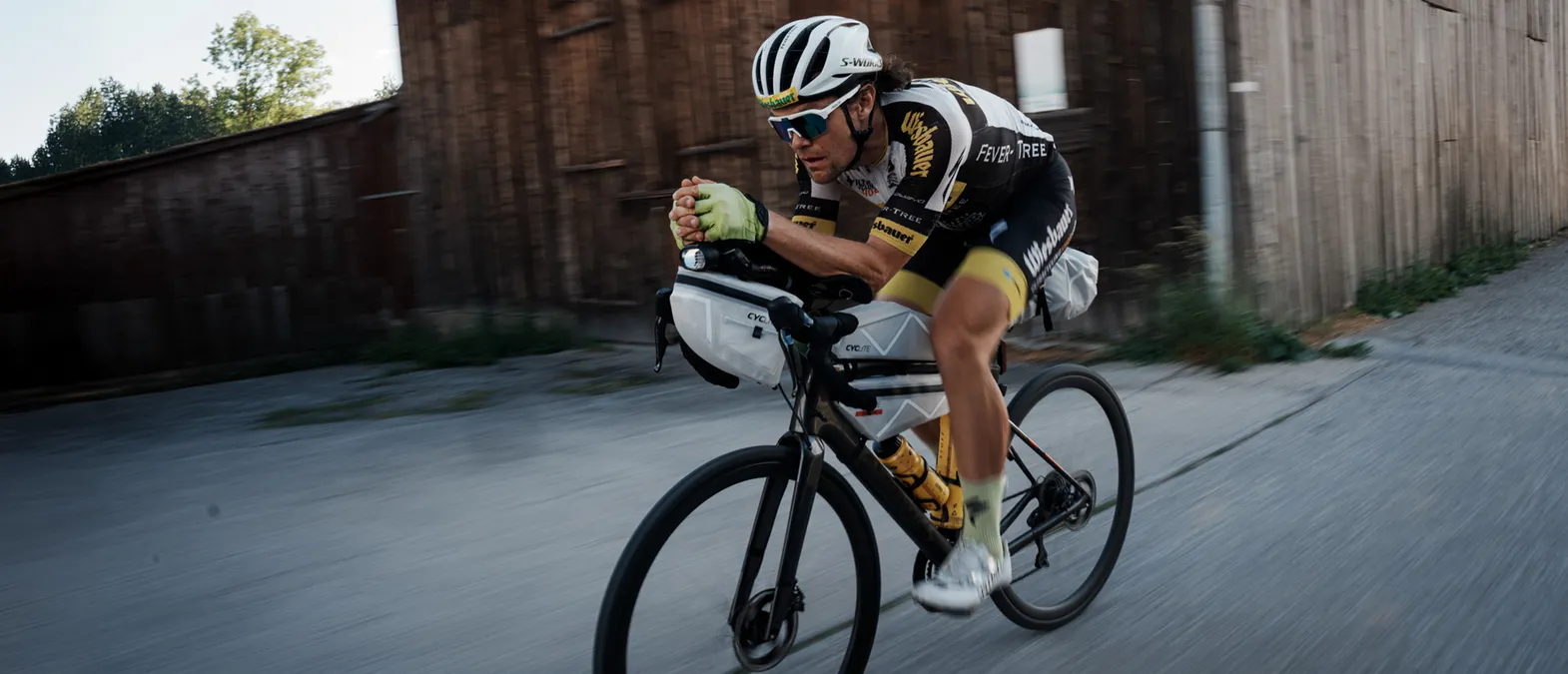 En syklist i en aerodynamisk posisjon på en veibrett, som bærer tilpasset sportsutstyr fra owayo, mens han sykler på en gate.