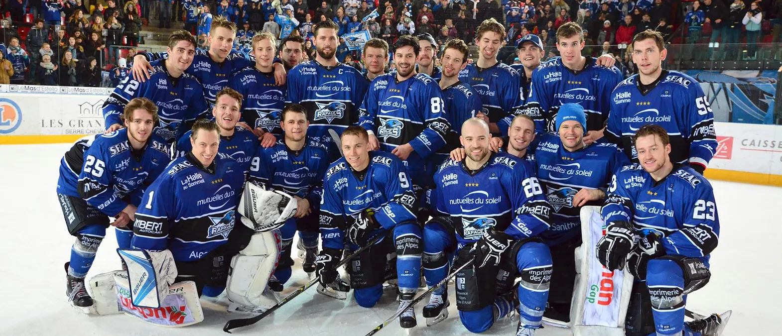 Et ishockeylag i blå trøyer med logoen til Rapaces de Gap poserer på isen foran et publikum.