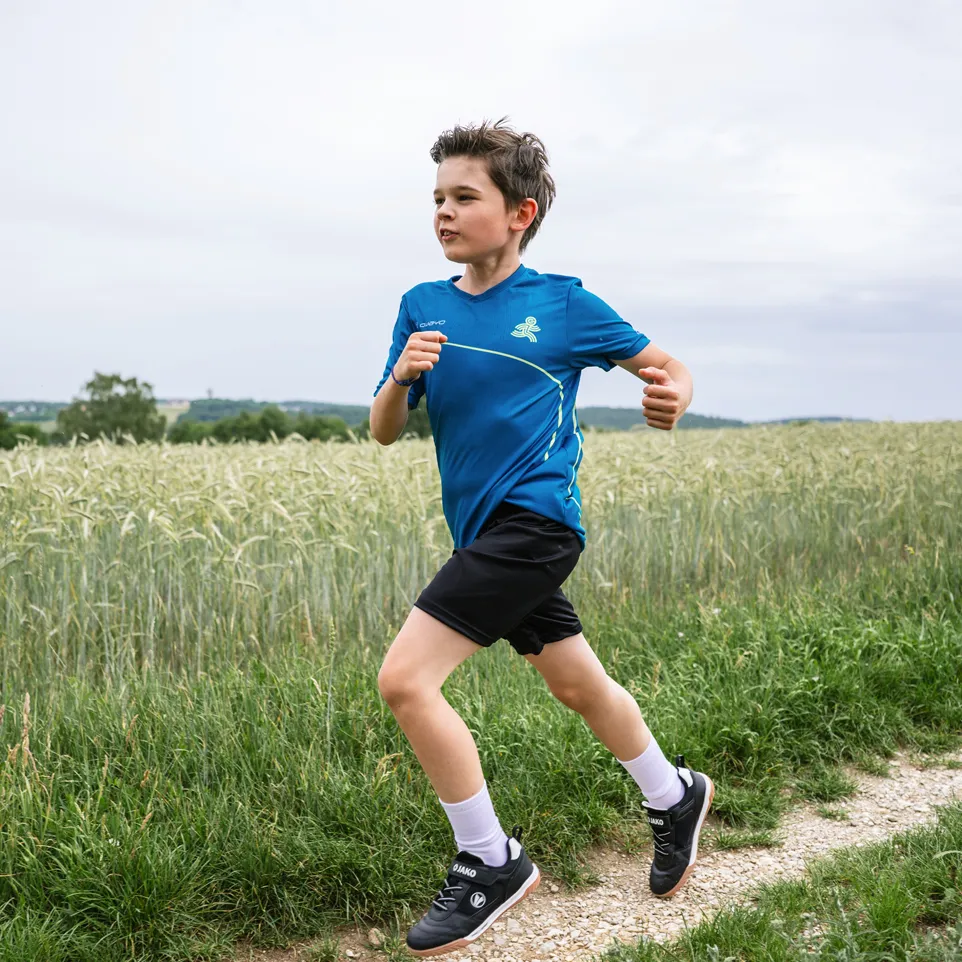 En gutt løper på en grusvei, iført en blå sportstrøye og svarte shorts.