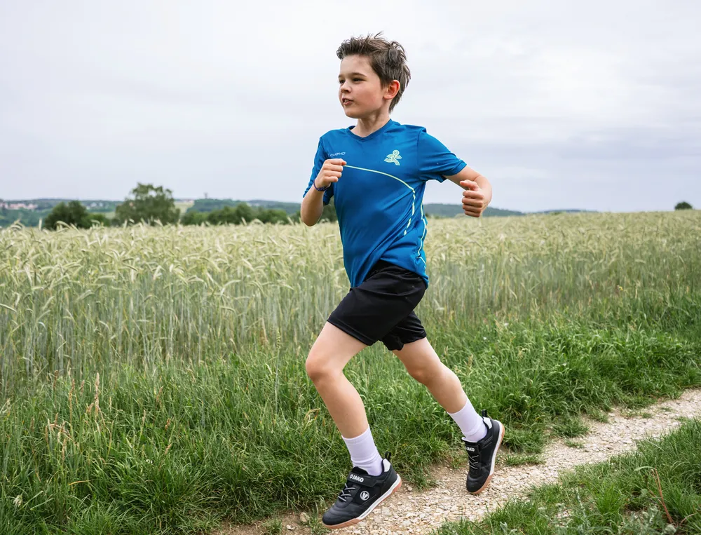 En gutt løper på en grusvei, iført en blå sportskjorte og svarte shorts.