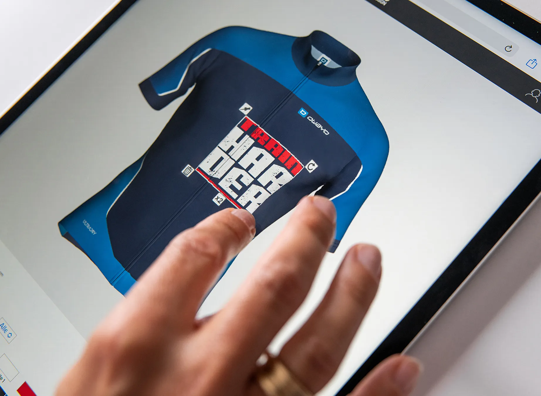 En hånd peker på et digitalt design av en blå sportsdrakt med teksten 'train harder'.