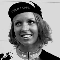 En kvinne med kort blondt hår bærer en svart sykkelkappe med teksten 'VELO LOVE' og et tilpasset sykkeltrøye med navnet 'Anja Sturm'.