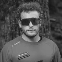 En mann med krøllete hår og solbriller bærer en grå, langærmet sportskjole med 'owayo'-logoen på skulderen og andre sponsorlogoer på brystet.