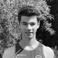 En ung mann i en svart og grå, ermeløs sportskjorte med 'owayo'-logoen på brystet, smiler foran en bakgrunn av grønne blader.