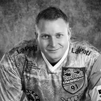 En mann i en sportslig, mønstret trøye med ulike sponsorlogoer, inkludert Red Bull og LaPati, og teksten 'owayo' på brystet.