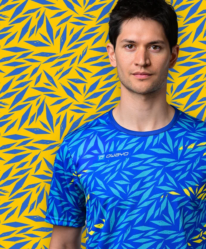 En ung mann har på seg en sporty blå T-skjorte med et fargerikt bladmønster mot en gul bakgrunn.