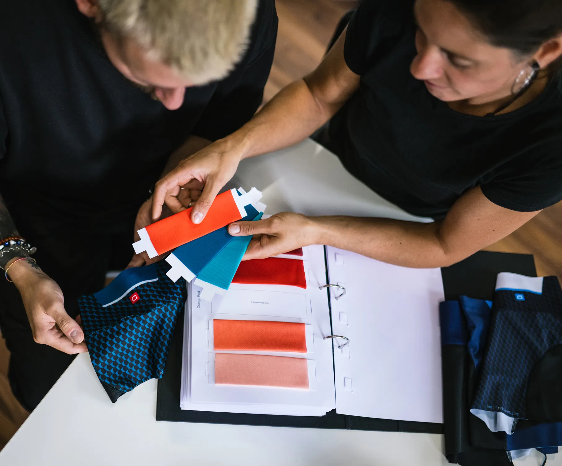 To personer velger farger for tilpasset sportstøy ved å se på stoffprøver og en fargekatalog.