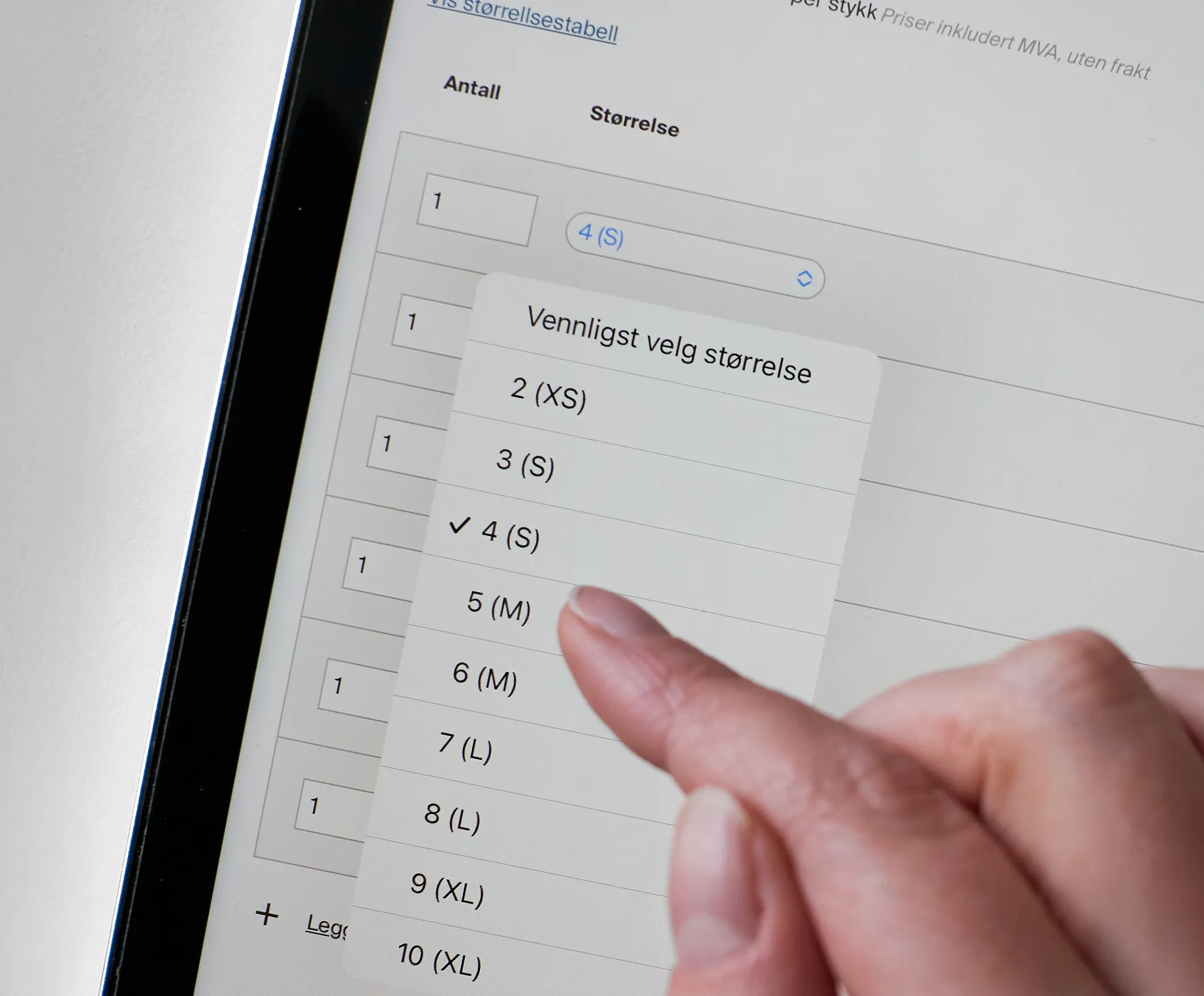En hånd velger størrelse 4 (S) fra et nedtrekksmeny på en tablet som viser en bestillingsside for tilpasset sportstøy.