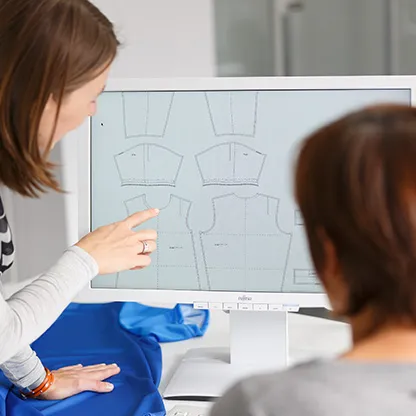 To personer ser på digitale mønstre for sportsklær på en dataskjerm, mens en person peker på skjermen.