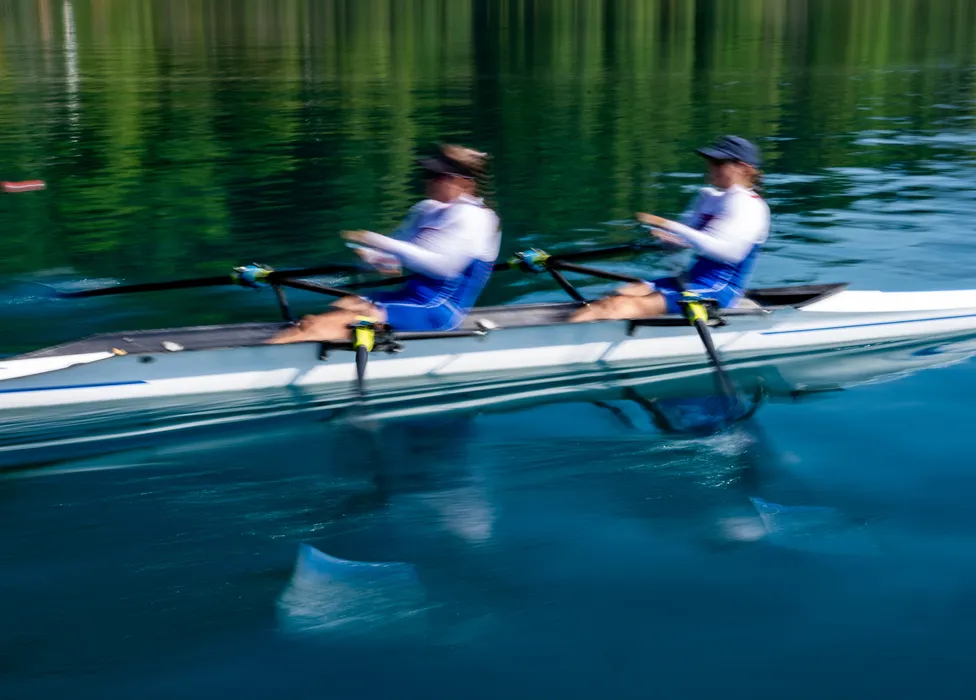 To roere i blå sportsklær ror synkront på rolig vann.