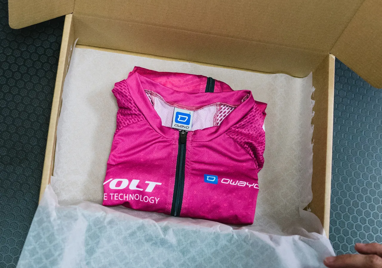 En foldet rosa, ærmeløs sportskjorte med owayo-logoen ligger i en pappeske på hvitt papir.