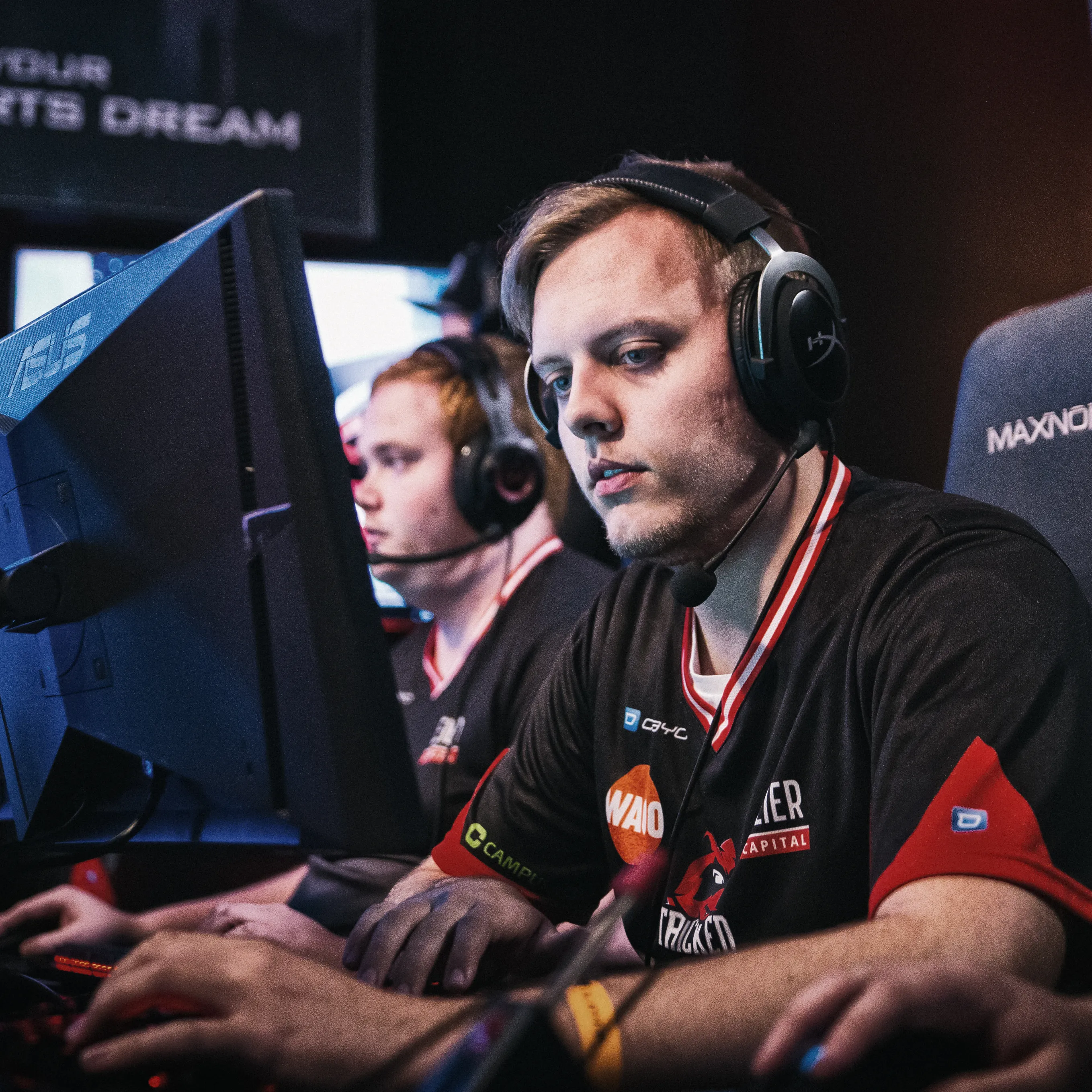 To spillere i sportslige T-skjorter med hodetelefoner, fokusert på datamaskinene sine under et eSports-turnering.