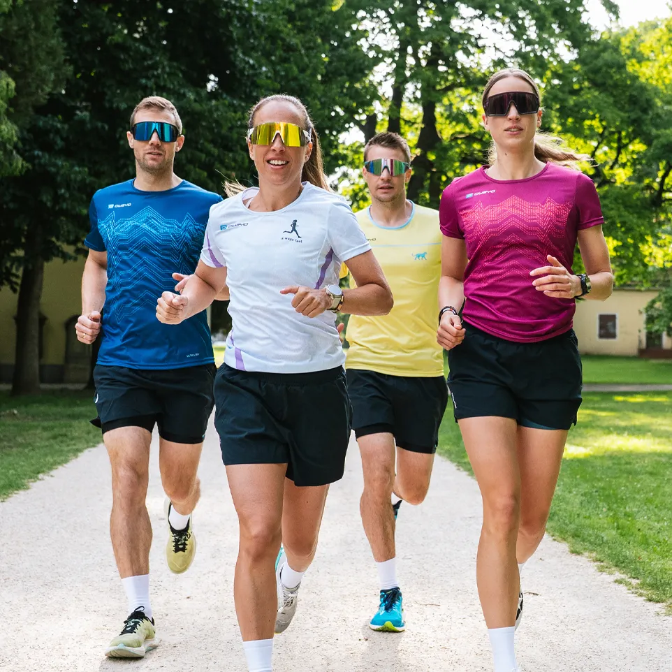 Fire løpere i fargerike sportstrøyer og shorts jogger på en sti i en park.
