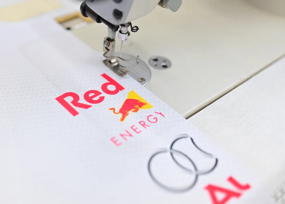 En syemaskin syr en hvit sportstøy med det røde Red Bull Energy-logoet og et annet logo.