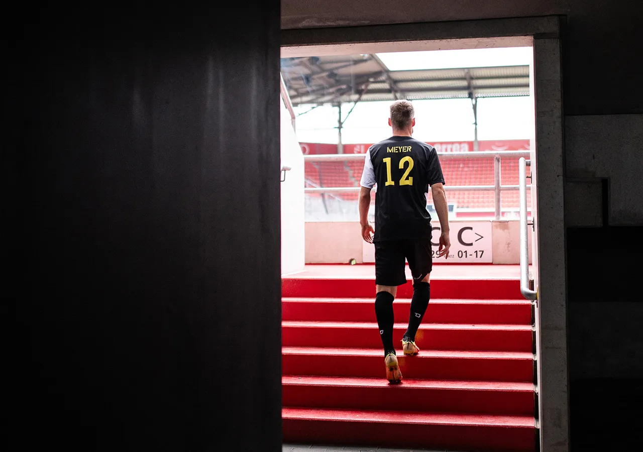 En fotballspiller med navnet Meyer og nummer 12 på ryggen går opp en rød trapp til et stadion.