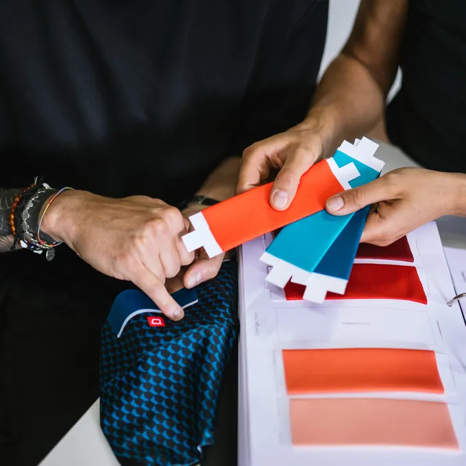 To personer velger fargeprøver for tilpasset sportsutstyr, med en blå stoff med mønster og ulike fargevarianter synlige.